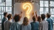 © AspctStyle - Large group of young professionals standing together in a modern office, pointing at a glowing neon question mark on the wall, symbolizing ideas and problem solving