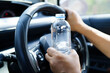 Asian woman driver holding water bottle in car.