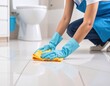 © Tasha - Person wearing blue gloves cleans the bathroom floor with a yellow cloth.