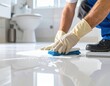 © Tasha - A person wearing gloves scrubs a white bathroom floor with a cleaning brush and product.