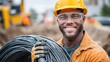 © NovaVision - Happy construction worker holding a coil of wire, smiling at the camera while on site.