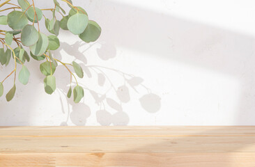 Wall Mural - Background for product presentation with wooden table and green eucalyptus leaves branch shadow on plaster wall