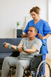© Xavier Lorenzo - Vertical shot of old man in wheelchair training with physiotherapist using dumbbells at home. Female therapist assisting senior man with exercises in nursing home service.