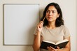 © Pixels Hunter - Thoughtful woman holding notebook and pencil beside blank whiteboard on wall, ideal for mockup or educational and planning design concepts. Ai generative