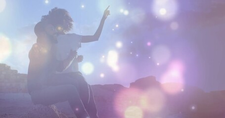 Wall Mural - animation of glowing spots of light over african american couple sitting on the rocks near the sea