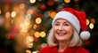 © oliamogdaleva - Portrait of a joyful senior woman in a Santa hat smiling happily with a festive, blurred lights in the background.