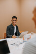 © Johnér - Happy young businessman sitting with laptop at table in office board room