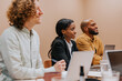 © Johnér - Smiling young female entrepreneur sitting with male colleagues in meeting room at office
