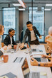 © Johnér - Young male business professional sticking adhesive note on table while discussing ideas with team in board room at office