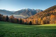 Melodic tunes over a lush green meadow with vibrant fall trees and towering mountains in the backdrop