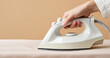 © Katerina Bond - Close-up of a woman's hand holding an electric steam iron while pressing fabric, illustrating household chores, cleanliness and garment care on a neutral background.