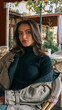 © shine.graphics - Portrait of a stylish young woman in a black ribbed turtleneck and beige trench coat, seated at an outdoor cafй with a calm, confident expression