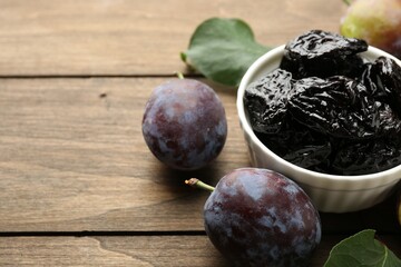 Wall Mural - Dried prunes, fresh plums and green leaves on wooden table, closeup. Space for text