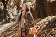 © deagreez - Charming young woman enjoying a sunny autumn day outdoors in a park with colorful foliage, wearing stylish warm clothing