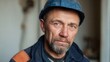© SerPak - A close-up portrait of a middle-aged male worker wearing a blue helmet, showcasing determination and experience in a construction environment.