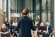© Maskot - Rear view of female delegate explaining strategies while giving lecture at summit to business people at congress center