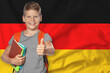 © New Africa - Little boy with backpack and notebooks showing thumbs-up against flag of Germany. Language school