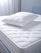 © Silvy - A close-up view of a white quilted mattress and pillow, showcasing a comfortable and inviting bedroom scene.