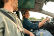 © Maskot - Smiling woman driving car while talking with man during road journey