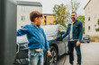© Maskot - Smiling man charging electric car while looking at son standing near kiosk
