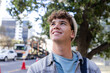© Wavebreak Media - Man looking upward on city sidewalk wearing denim jacket, knit beanie, backpack