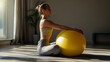 © Narmin - Woman lifting a yellow exercise ball while sitting on a yoga mat, representing strength and balance