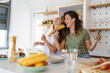 © Dorde - Cheerful Female Friends Having Fun Singing With Phone As Microphone During Morning Meal Preparation In Sunlit Kitchen