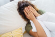 © Dorde - Tired Woman With Natural Curly Hair Lying Down On Bed Covering Face With Hands In Bright Bedroom