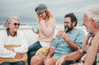 © luciano - Cheerful multi-generation family laughing having fun together sitting outside on terrace. Couple of parents with grandparents enjoying free time