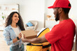 © Prostock-studio - Food Delivery Concept. Positive black courier guy taking cardboard box from yellow thermal backpack and giving it to smiling customer, delivering order from restaurant, woman taking carton package