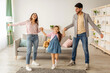 © Prostock-studio - Home entertainment. Joyful arab family dancing to music with his cute daughter. Happy girl, father and mother having fun, enjoying time together at home in living room interior