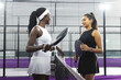 © Wavebreak Media - Diverse female friends standing at net on enclosed padel court with paddles discussing next play