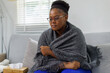 © David - African American woman wrapped on a couch,in a blanket, with flu virus blowing her nose at home.She appears to be sick or to have allergies.
