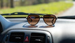 © Anastasia - Sunglasses resting on dashboard of car with green landscape outside