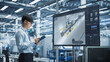 © Gorodenkoff - Smart Factory Innovation: Asian Engineer Analyzes Concept of Automated Production Line on Large Screen TV Screen. Using Digital Tablet Computer He Optimizes Manufacturing in Industrial Facility