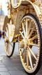 © nur - A close-up shows the intricate golden wheels, adorned with pearls, of a regal carriage against a blurred city background, evoking luxury and historical charm