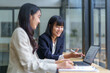 © amnaj - Two asian businesswomen are discussing and analyzing data on a laptop in a modern office, collaborating on a project and sharing ideas