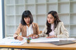 © amnaj - Two asian businesswomen reviewing financial data, pointing at charts and graphs while working together on a project in a modern office