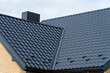 © SMK - Dark grey metal roof tiles on a modern house with chimney and light brick wall.