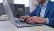 © zian - A man in a blue blazer types on a laptop at a clean, white desk. An office telephone and screens are softly focused in the background