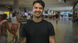 © Krakenimages.com - Young hispanic man gesturing come here with hands smiling in a busy indoor airport setting surrounded by travelers and luggage during a lively day.