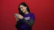 © Krakenimages.com - Woman with brunette hair in purple volunteer shirt using smartphone against red background