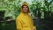 © Krakenimages.com - Hispanic man in yellow raincoat stands with crossed arms in a lush outdoor park, surrounded by greenery, showcasing a confident and thoughtful demeanor amid nature's vivid backdrop.
