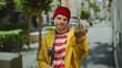 © Krakenimages.com - Young man displaying middle finger in urban street with fishing rod and yellow jacket, red beanie, and striped shirt.