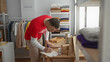 © Krakenimages.com - Young man in a volunteer shirt organizes clothes and packages in a charity donations room, focusing intently on his task.