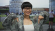 Woman pointing outdoors near pisa tower with glasses and floral blouse, surrounded by tourists in italian cityscape, expressing happiness and curiosity in historic urban setting.
