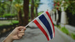 Hand of a person holding thai flag on a sunny street in thailand, showcasing patriotism in a vibrant outdoor urban setting.