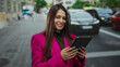© Krakenimages.com - Woman in pink blazer using tablet on busy street captures urban essence with technology and confidence amid city hustle.