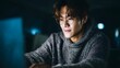 © Thares2020 - Young person wearing glasses diligently works on a laptop in a dimly lit modern indoor setting illuminated by the screen s glow