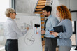 © Novak - Business team during a presentation in the office. A woman is pointing at a flipchart with bar and pie charts, while two colleagues listen attentively and take notes.